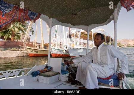 Un uomo egiziano vele il suo motore assistito feluca sul Nilo ad Aswan, Egitto. Foto Stock