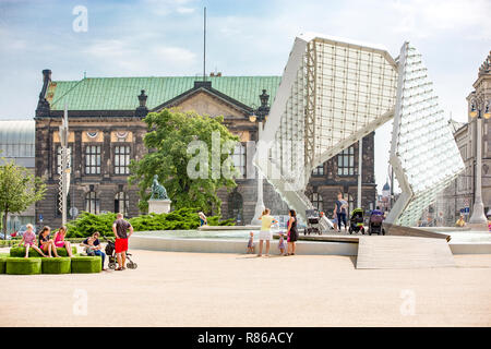 La Polonia, Poznan, persone con una chat e appoggiata dalla moderna fontana sulla piazza te "Plac Wolnosci' a Poznan. Museo Nazionale in background. Foto Stock