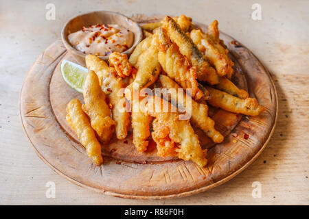 Fritte bianchetti spratti servita in una croccante pastella dorata su un tagliere di legno che serve la scheda con una fetta di limone e un piccolo piatto di salsa al peperoncino un Foto Stock