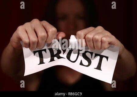Strappato carta bianca con disegnato lettere di 'fiducia'. Ragazza strappando la carta in due metà. Foto Stock