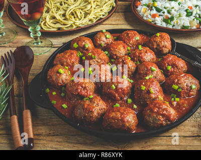 In casa le polpette di carne in salsa di pomodoro. Padella su una superficie in legno, riso con verdure, pasta Foto Stock