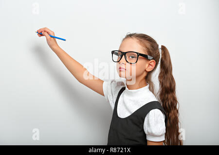 Smart pupilla kid ragazza in occhiali guardando sulla parete blu lo sfondo con il disegno a matita e pensando a Foto Stock