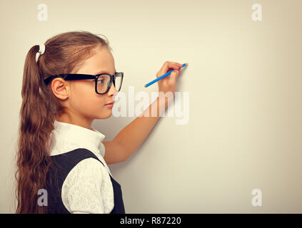 Smart pupilla kid ragazza in occhiali guardando sulla tonica vintage colore sfondo a parete con disegno a matita e pensando a Foto Stock