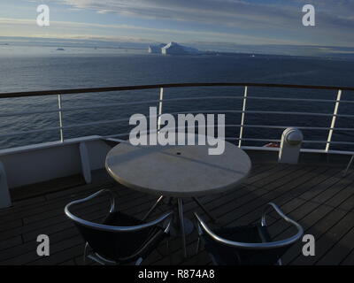 Ilulissat Eisberge am Abend Zwei leere Stühle vor einem leeren Tisch auf dem Deck eines Kreuzfahrtschiffes mit Blick auf die eisige Kulisse, Foto Stock