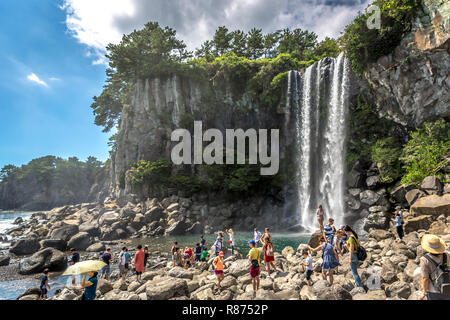 Jeju Island, Corea del Sud - Settembre XV 2018 - un grande gruppo di persone aventi il divertimento nelle rocce di fronte ad una cascata in un cielo blu giorno di Jeju Island, Sout Foto Stock
