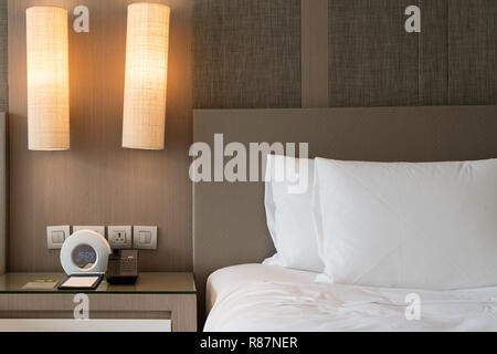 Close up frammento di camera da letto con lampada da lettura e sveglia digitale in casa moderna o hotel. Foto Stock