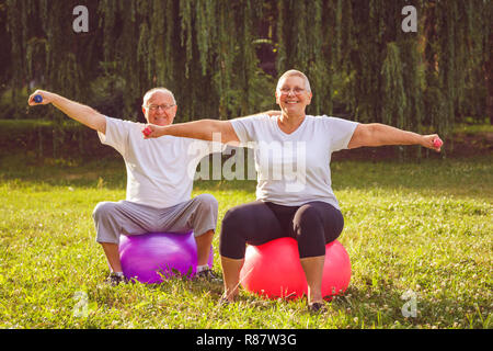 Esercizio Senior - pensionato sorridente giovane facendo esercizi di fitness sulla sfera di fitness in posizione di parcheggio Foto Stock