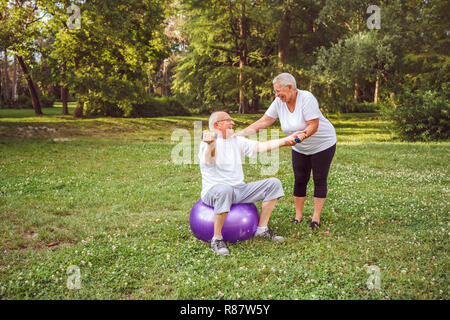 Fare insieme gli esercizi di fitness sulla sfera di fitness nel parco concetto di uno stile di vita sano esercizio Senior - sorridente coppia uomo e donna Foto Stock