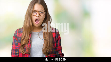 Giovane bella bruna donna in giacca e occhiali su sfondo isolato in shock viso, cercando scettici e sarcastico, sorpreso con open Foto Stock