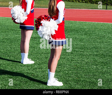 Due high school cheerleaders sono in piedi all attenzione con i loro pompon dietro di loro ottenere pronto per iniziare la loro routine. Foto Stock