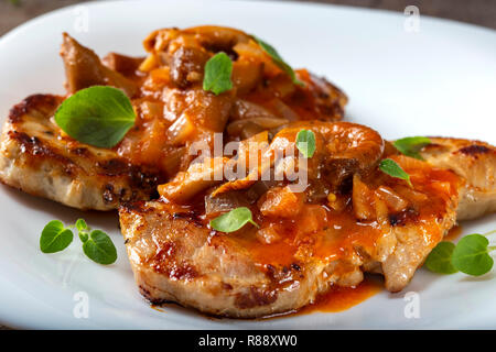 Fritte costolette di maiale con salsa di verdure ed erbe su una piastra bianca Foto Stock