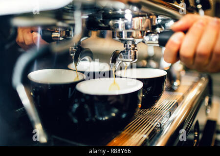 Close up e vista di taglio di mano d'uomo azienda cezve dalla macchina da caffè al di sopra di due tazze. Il caffè viene colata fuori da esso in tazze Foto Stock