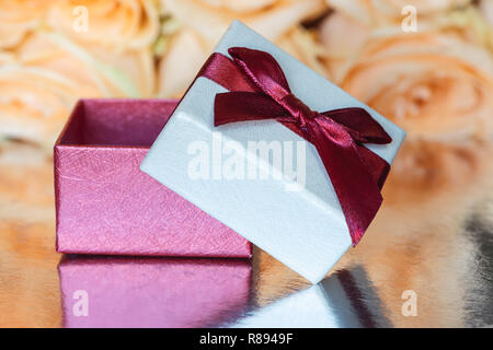 La confezione regalo è su una superficie di argento su sfondo giallo di rose. Foto Stock