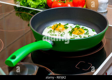 Coppa verde con uova strapazzate da due uova su un fornello in cucina Foto Stock