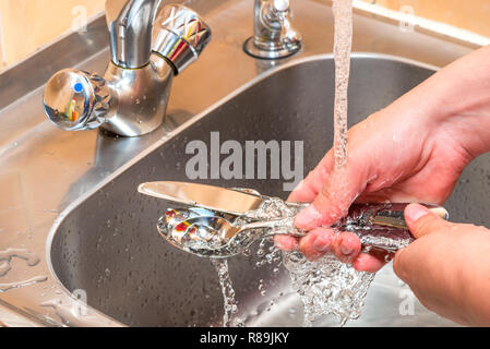 Mani close up - posate di lavaggio sotto acqua corrente in cucina Foto Stock