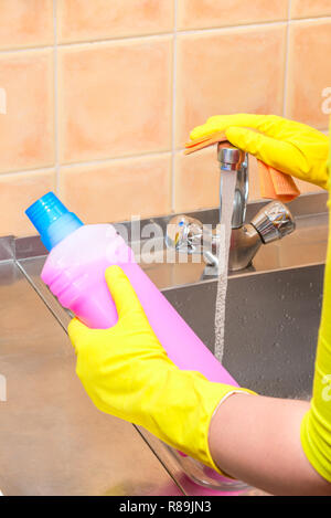 Mano con uno straccio e prodotti per la pulizia in cucina durante la pulizia Foto Stock