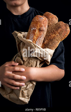 Pane appena sfornato baguette nella craft sacchetto di carta in il ragazzo con le mani in mano. Cibo scuro foto. Stile rustico. Messa a fuoco selettiva. Foto Stock