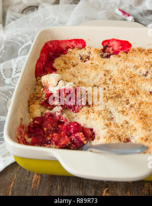 Crumble con fragole e rabarbaro in piatto di ceramica su un tavolo di legno. Foto Stock