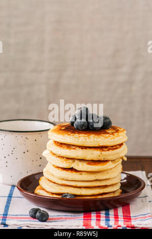 Pila di Pancake fatti in casa con i mirtilli in una piastra, latte in un vaso, in stile rustico. Copia dello spazio. Foto Stock