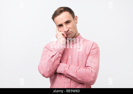 Cupo uomo in maglia rosa, tenendo le mani sul viso, accigliata e fissando con espressione impotente Foto Stock