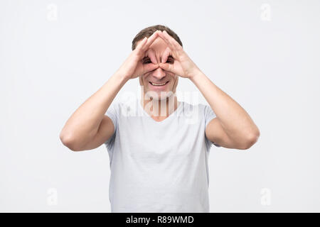 Giovane uomo che mostra il gufo segno con le dita. Rendere divertente grimace. Foto Stock