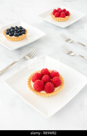 In casa di lampone e mirtillo canapes riempito con crema vaniglia su porcellana bianca lastre di marmo bianco e lo sfondo. Foto Stock