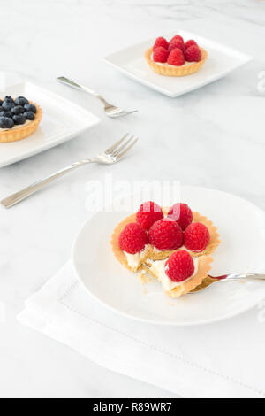 In casa mirtillo e lampone pasticcini riempiti con crema vaniglia su porcellana bianca lastre di marmo bianco e lo sfondo. Foto Stock