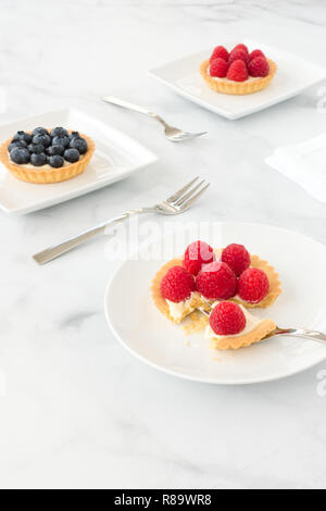 In casa mirtillo e lampone pasticcini riempiti con crema vaniglia su porcellana bianca lastre di marmo bianco e lo sfondo. Foto Stock