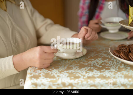 Vista dettagliata della delicata tazza di caffè in piedi su una piastra. Donna con le mani in mano e la tazza di caffè sul tavolo. Foto Stock