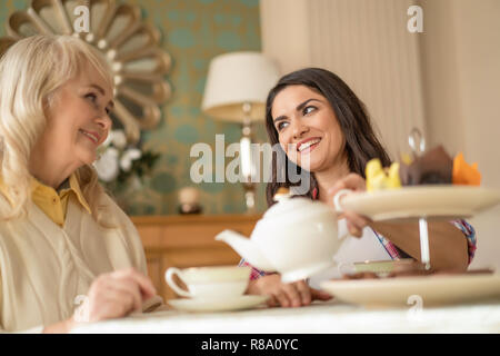 Sorridente donna affascinante ha una grande conversazione con il suo grazioso madre sulla tazza di tè a casa Foto Stock