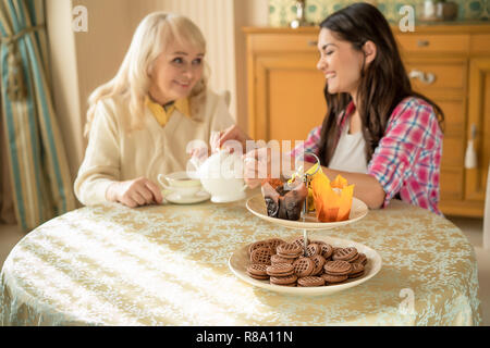 Cavalletto di dessert con biscotti e tortine in primo piano. Inquadratura sfocata di sorridere le donne impegnati in una conversazione mentre è seduto al tavolo sulla BAC Foto Stock