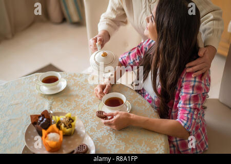 Ritagliato colpo di donna anziana versando tè aromatico da Wtire teiera ceramica nella ragazza in tazza. Family Colazione Foto Stock