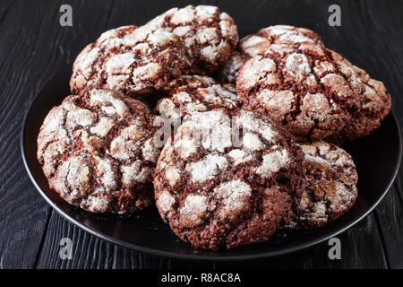 Close-up di Chocolate Crinkle cookies. Incrinato biscotti al cioccolato. Biscotti al cioccolato, biscotti di Natale su un piatto nero su un tavolo di legno, Horizon Foto Stock