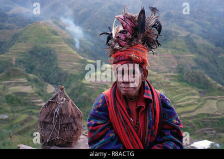 Un anziano uomo Ifugao indossare copricapo ornato con piume e monkey cranio al Banaue terrazze di riso nel nord di Luzon, Filippine. In passato gli Ifugao noto anche come Ifugaw, Ipugao, Yfugao temevano erano cacciatori di teste, così come altre tribù delle regioni montuose del Luzon del nord. Foto Stock