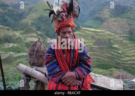 Un anziano uomo Ifugao indossare copricapo ornato con piume e monkey cranio al Banaue terrazze di riso nel nord di Luzon, Filippine. In passato gli Ifugao noto anche come Ifugaw, Ipugao, Yfugao temevano erano cacciatori di teste, così come altre tribù delle regioni montuose del Luzon del nord. Foto Stock