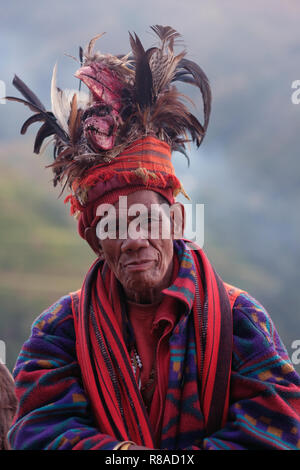 Un anziano uomo Ifugao indossare copricapo ornato con piume e monkey cranio al Banaue terrazze di riso nel nord di Luzon, Filippine. In passato gli Ifugao noto anche come Ifugaw, Ipugao, Yfugao temevano erano cacciatori di teste, così come altre tribù delle regioni montuose del Luzon del nord. Foto Stock