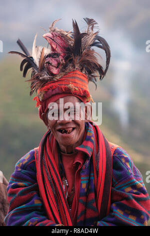 Un anziano uomo Ifugao indossare copricapo ornato con piume e monkey cranio al Banaue terrazze di riso nel nord di Luzon, Filippine. In passato gli Ifugao noto anche come Ifugaw, Ipugao, Yfugao temevano erano cacciatori di teste, così come altre tribù delle regioni montuose del Luzon del nord. Foto Stock