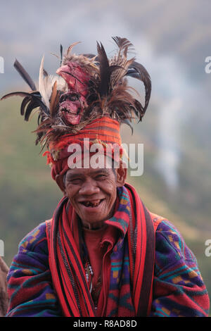 Un anziano uomo Ifugao indossare copricapo ornato con piume e monkey cranio al Banaue terrazze di riso nel nord di Luzon, Filippine. In passato gli Ifugao noto anche come Ifugaw, Ipugao, Yfugao temevano erano cacciatori di teste, così come altre tribù delle regioni montuose del Luzon del nord. Foto Stock