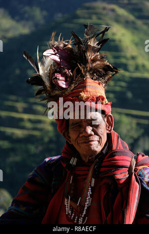 Un anziano uomo Ifugao indossare copricapo ornato con piume e monkey cranio al Banaue terrazze di riso nel nord di Luzon, Filippine. In passato gli Ifugao noto anche come Ifugaw, Ipugao, Yfugao temevano erano cacciatori di teste, così come altre tribù delle regioni montuose del Luzon del nord. Foto Stock