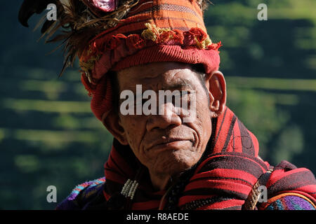 Un anziano uomo Ifugao indossare copricapo ornato con piume e monkey cranio al Banaue terrazze di riso nel nord di Luzon, Filippine. In passato gli Ifugao noto anche come Ifugaw, Ipugao, Yfugao temevano erano cacciatori di teste, così come altre tribù delle regioni montuose del Luzon del nord. Foto Stock