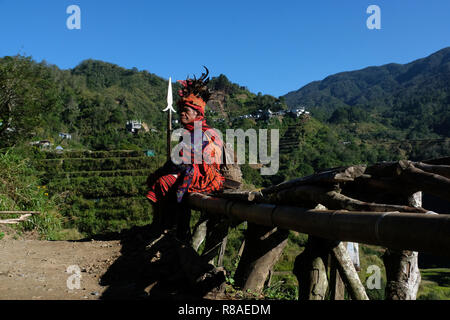 Un anziano uomo Ifugao indossare copricapo ornato con piume e monkey cranio al Banaue terrazze di riso nel nord di Luzon, Filippine. In passato gli Ifugao noto anche come Ifugaw, Ipugao, Yfugao temevano erano cacciatori di teste, così come altre tribù delle regioni montuose del Luzon del nord. Foto Stock