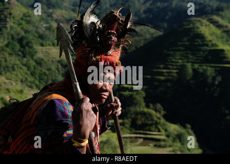 Un anziano uomo Ifugao indossare copricapo ornato con piume e monkey cranio al Banaue terrazze di riso nel nord di Luzon, Filippine. In passato gli Ifugao noto anche come Ifugaw, Ipugao, Yfugao temevano erano cacciatori di teste, così come altre tribù delle regioni montuose del Luzon del nord. Foto Stock