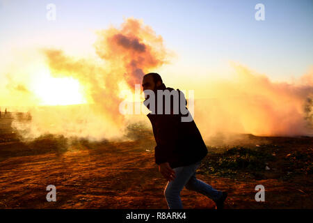 Dicembre 14, 2018 - Gaza, Palestina - un uomo palestinese visto con un gas lacrimogeni granata in mano al tramonto durante gli scontri tra i cittadini palestinesi e le forze israeliane nel nord della Striscia di Gaza nel corso di una protesta contro il riconoscimento del Presidente americano Trump, Gerusalemme come capitale di Israele. (Credito Immagine: © Ahmad Hasaballah/SOPA immagini via ZUMA filo) Foto Stock