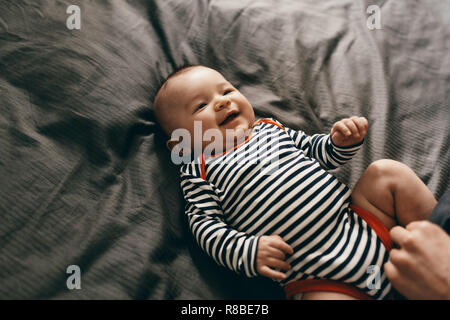 Vista dall'alto di un sorridente neonato sdraiato sul letto. Allegro piccolo bambino in un giocoso umore giacente sul letto. Foto Stock