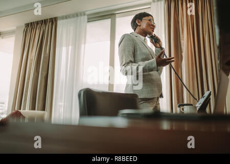 Imprenditrice di effettuazione della chiamata dalla camera dell'albergo. Imprenditrice in formali più di parlare di telefono su rete fissa, funzionante da camera in hotel durante un viaggio d'affari. Foto Stock