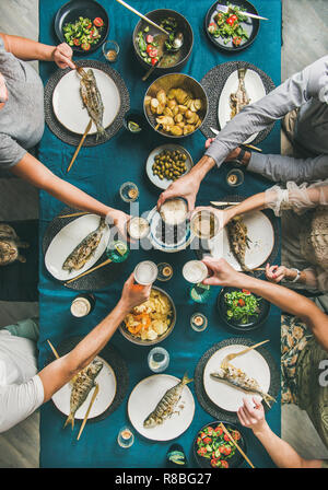 Pesce, patatine, birra party raduno di amici di mangiare e di bere e festeggiare. Flat-lay di mani umane, bicchieri da birra, branzino grigliato pesci, vegetab Foto Stock