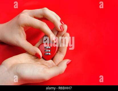 Lucchetto a cuore in forma le mani delle donne contro uno sfondo di seta rossa Foto Stock