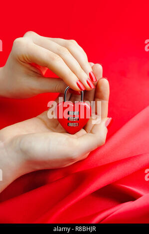 Lucchetto a cuore in forma le mani delle donne contro uno sfondo di seta rossa Foto Stock