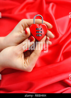 Lucchetto a cuore in forma le mani delle donne contro uno sfondo di seta rossa Foto Stock