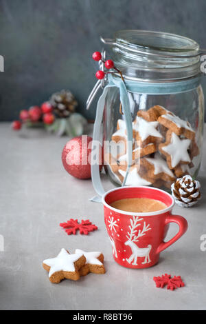 Sfondo di natale con caffè in rosso Xmas cup e stella gustosi biscotti allo zenzero in un vasetto di vetro con decorazioni di inverno Foto Stock